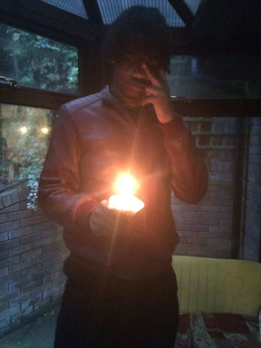 yukan in the dark at night, holding a small flame up to his face